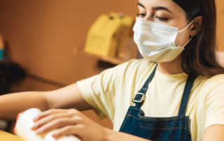 A teenager in a mask is working a job while standing at a tall desk